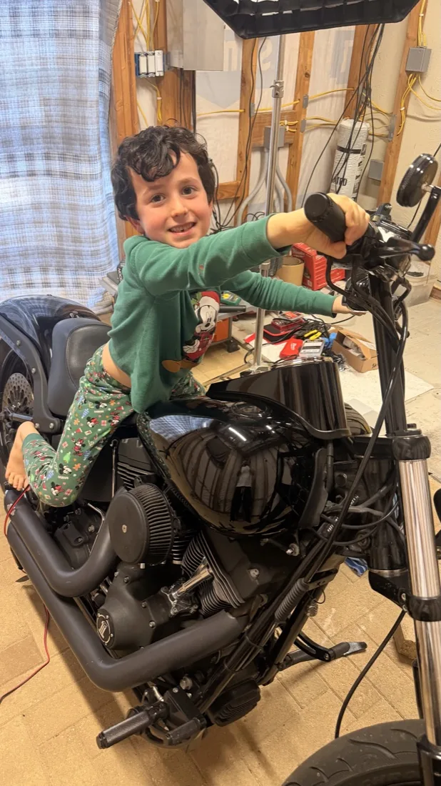A smiling young boy sitting on a black Harley-Davidson Night Train