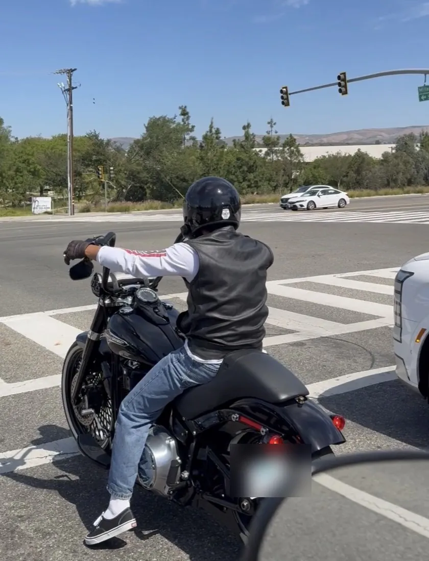 Johnny stopped at a red light on his Harley wearing a helmet, leather vest, and gloves
