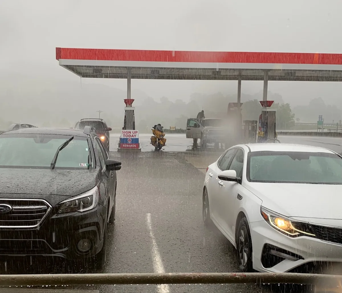 A lone motorcycle out in heavy rain at a gas station while cars shelter