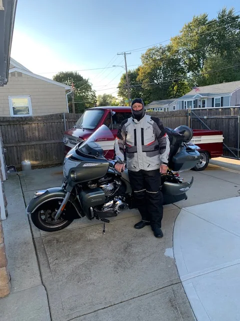 Rider in layered cold-weather gear and a balaclava beside a gray Indian touring motorcycle