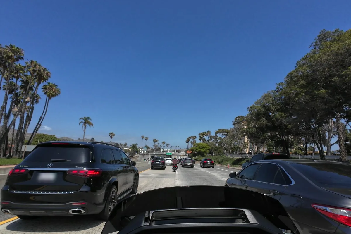 Motorcycle view of the gap between a black Mercedes SUV and a sedan while lane splitting in slow California freeway traffic